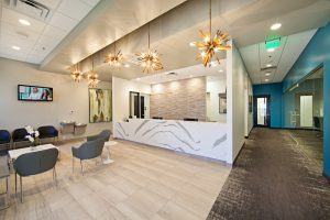 Modern dental office reception area with white desk, blue chairs, and chandeliers