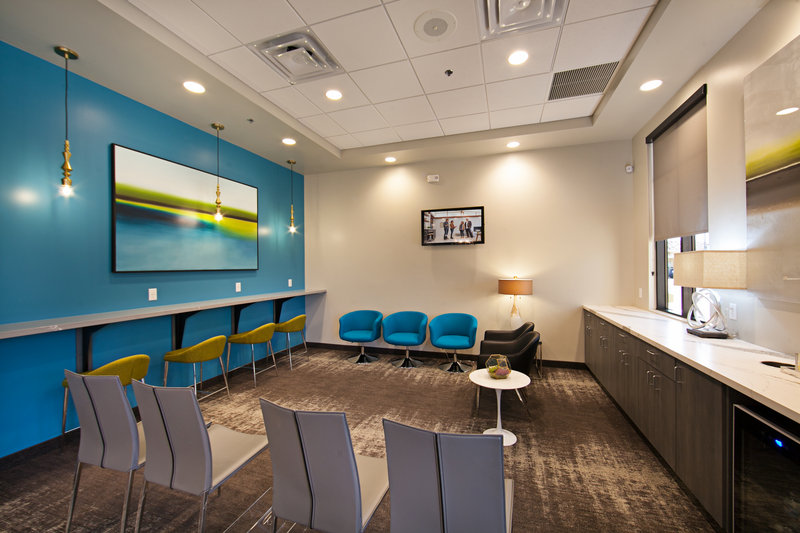 Dental waiting area with blue/yellow chairs, counter, and blue wall with painting
