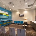 Dental waiting area with blue/yellow chairs, counter, and blue wall with painting