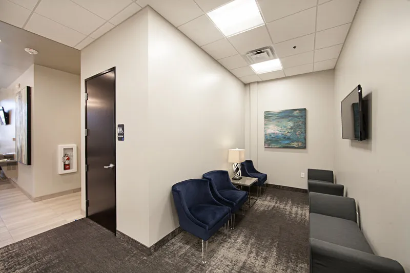 Dental waiting room with blue chairs, door, and wall painting