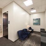 Dental waiting room with blue chairs, door, and wall painting