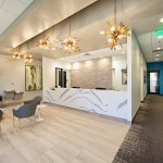 Modern dental office reception area with white desk, blue chairs, and chandeliers