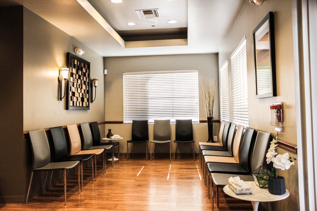 Dental waiting room with chairs, wooden floor, wall art, and window with blinds
