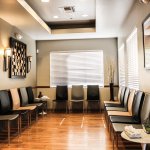 Dental waiting room with chairs, wooden floor, wall art, and window with blinds