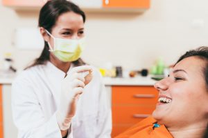 Dental professional in mask and white coat showing tool to patient in orange bib